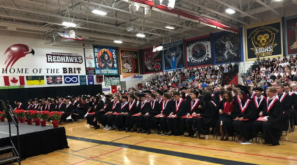 Studenti in toga alla cerimonia di diploma del Bedford Road Collegiate si trovano in una palestra.
