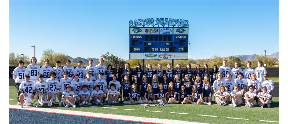 Jugadoras y jugadores de fútbol de Cactus Shadows High School están en el campo frente a un marcador con montañas al fondo.