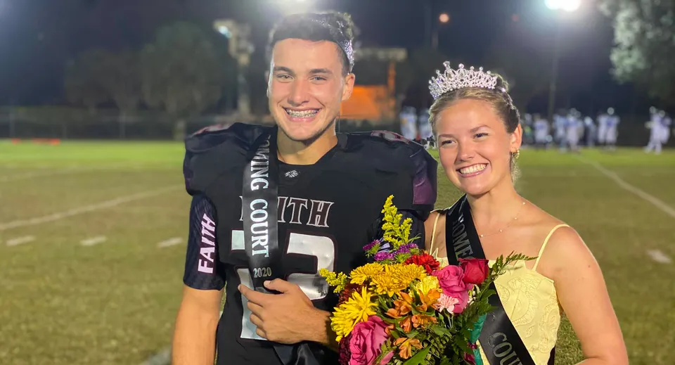 Un uomo in maglia da calcio sta accanto a una donna con corona e fiori sul campo da calcio della Faith Christian Academy in Florida.