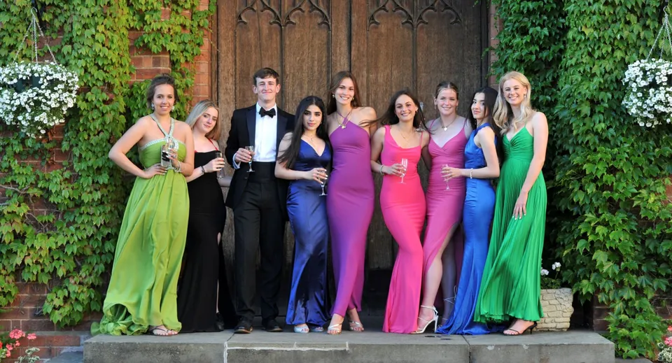 Un gruppo di persone vestite in modo elegante in posa davanti a una porta di legno circondata da piante verdi nei giardini della Dean Close School.