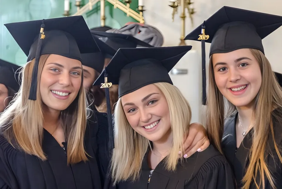 Tre studentesse della École Secondaire Augustin-Norbert-Morin in abito da diploma posano insieme sul campus.
