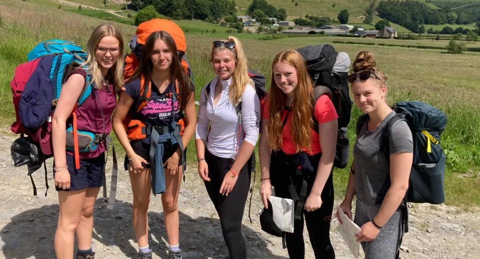 Un gruppo di studentesse del Wrekin College sta in abbigliamento da trekking in un ambiente panoramico con colline e alberi.