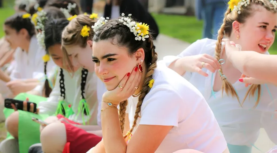 Un gruppo di giovani donne con abiti bianchi e corone di fiori si trova su un prato nel campus della Emma Willard School.