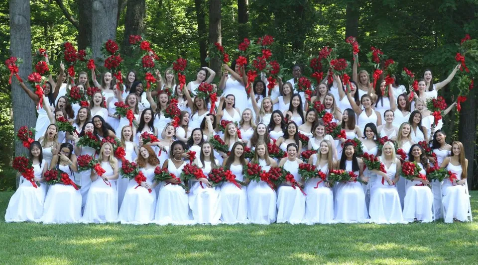 Un gruppo di studentesse della The Madeira School sta nel bosco e tiene delle rose rosse.