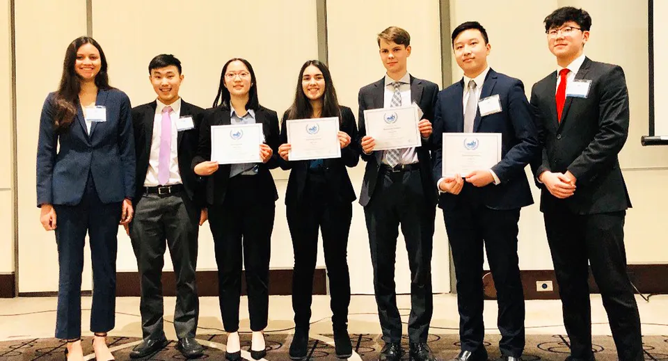 Studenti della Kitsilano Secondary School in abiti formali con certificati davanti a uno sfondo neutro.