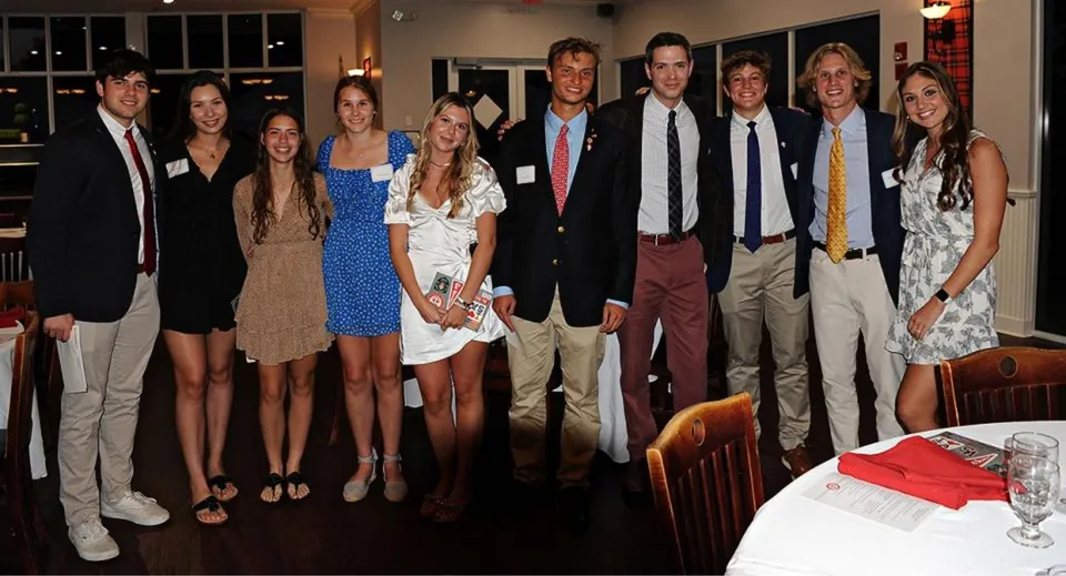 Un gruppo di persone si trova a un evento della Saint Andrews School in una sala formale con divani.