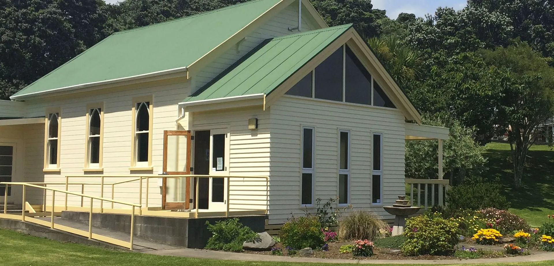 Una deliziosa casa in legno con un tetto in metallo verde si trova tra gli alberi e un giardino curato all'interno del campus del Sacred Heart Girls' College a New Plymouth.