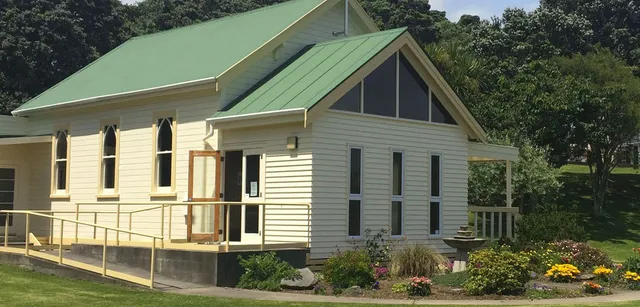 Una deliziosa casa in legno con un tetto in metallo verde si trova tra gli alberi e un giardino curato all'interno del campus del Sacred Heart Girls' College a New Plymouth.