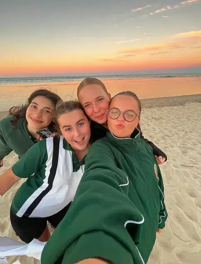 Studentesse in divisa scolastica si fanno un selfie su una spiaggia al tramonto in Australia