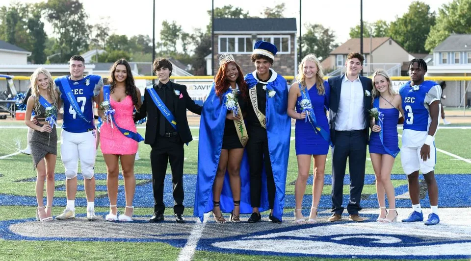 Un gruppo di diplomati e diplomate della Conwell-Egan Catholic High School si trova su un campo sportivo con edifici e alberi sullo sfondo.