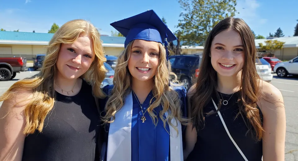 Tre studentesse della Langley Fundamental Middle and Secondary School sorridono insieme a una cerimonia di diploma all'aperto.