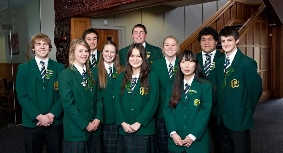 Un gruppo di studenti in uniforme scolastica verde si trova insieme in un corridoio della Papanui High School.