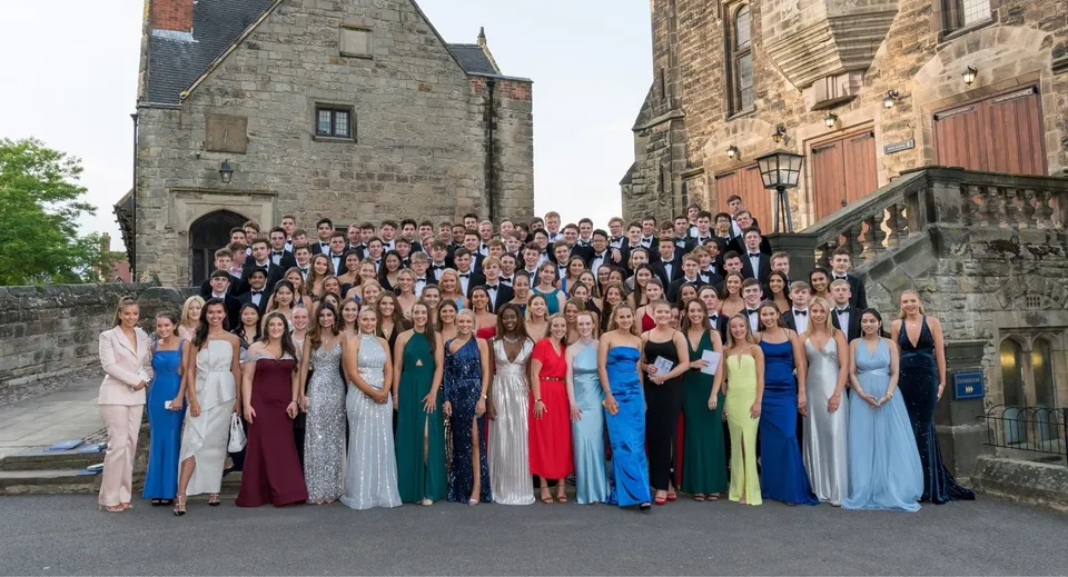 Un grande gruppo di studentesse in abito formale è in piedi davanti allo storico edificio in pietra nel campus della Repton School.
