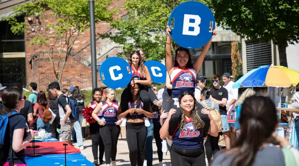 Un gruppo di studenti tiene cartelli colorati davanti all'edificio in mattoni del Brookdale Community College in una giornata di sole.