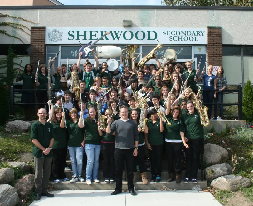 Banda escolar con instrumentos y profesores delante de la entrada de la Sherwood Secondary School