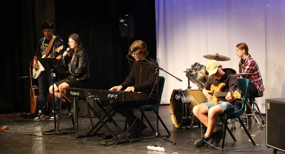 Un gruppo di musiciste e musicisti della Wellington Point State High School si esibisce sul palco con diversi strumenti.