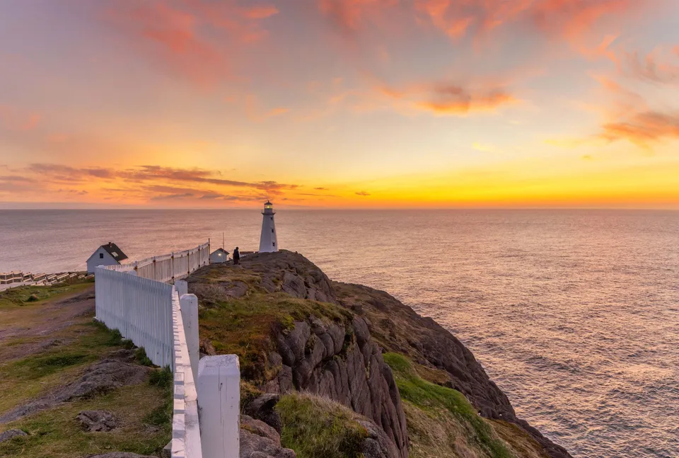 Un faro si erge su una scogliera rocciosa con vista sul mare al tramonto vicino alla Waterford Valley High School.