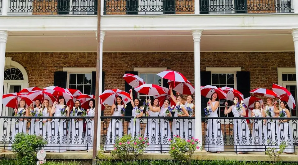 Un gruppo di studenti e studentesse con ombrelli colorati si trova sul balcone di un edificio in mattoni della Academy of the Sacred Heart.