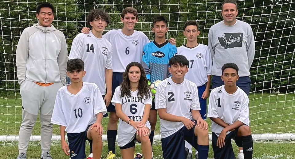 Un gruppo di studenti della Lawrence Woodmere Academy posa insieme sul campo da calcio davanti alla porta.