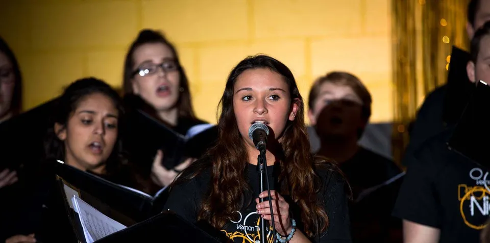 Studenti della Vernon Township High School cantano insieme su un palco con sfondo giallo.