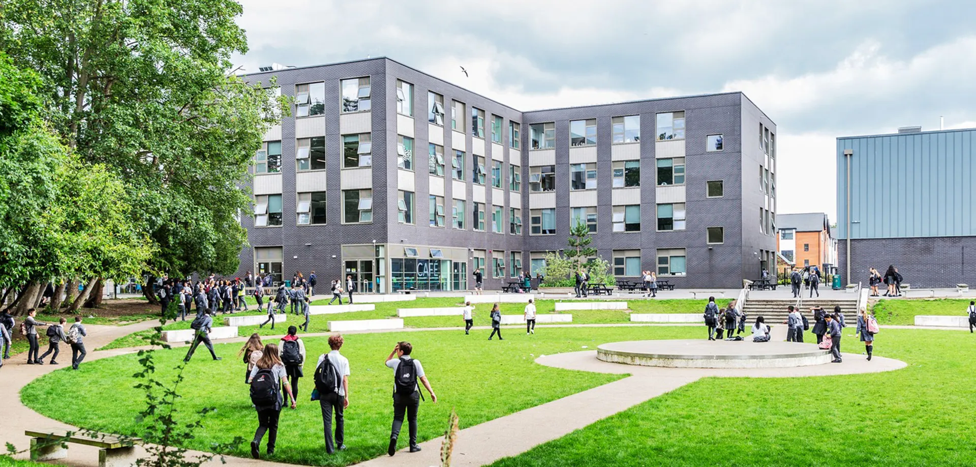 Studenti e persone nel cortile erboso davanti al moderno edificio della The Wren School.