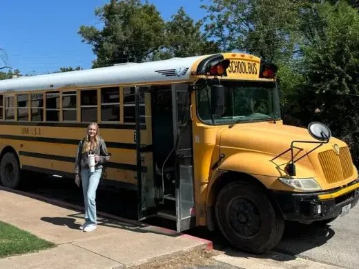 Studentessa sorridente accanto a uno scuolabus giallo americano