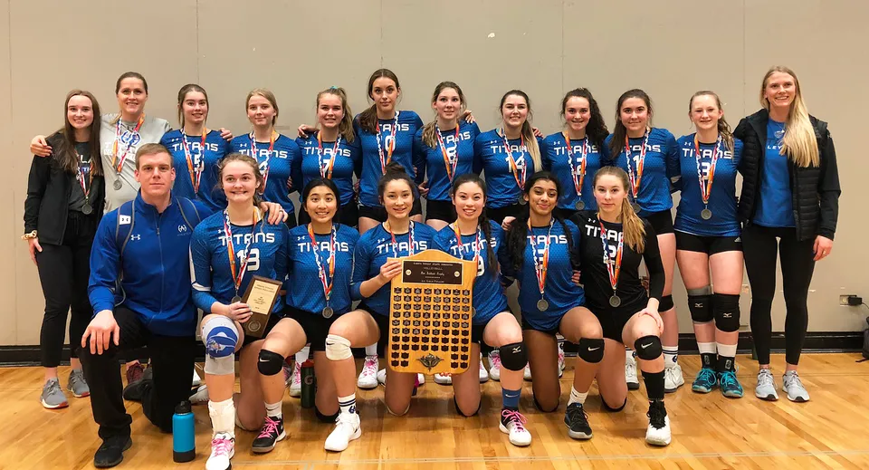 Studentesse della Harry Ainlay High School tengono insieme un trofeo di pallavolo sul pavimento della palestra.