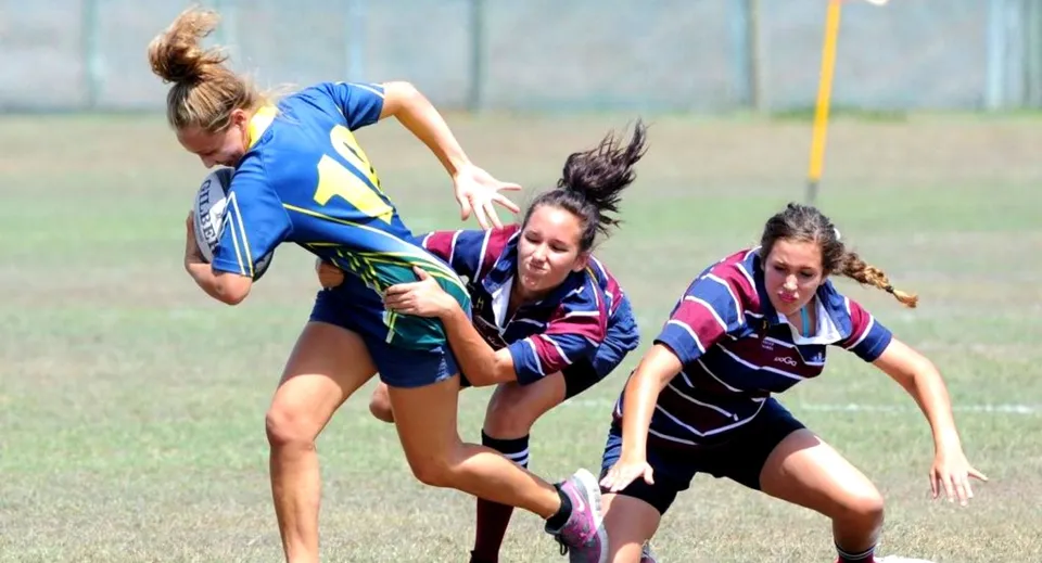 Tre studentesse del Fraser Coast Anglican College partecipano a una competizione sportiva su un campo d'erba.