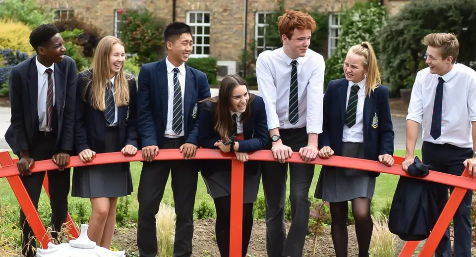 Un gruppo di studenti della Pocklington School si trova su un ponte rosso all'aperto davanti a un edificio in mattoni.
