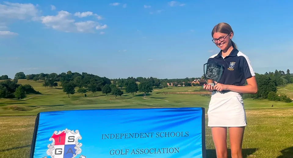 Una studentessa di Reddam House Berkshire in uniforme scolastica si trova su un campo da golf con alberi e colline sullo sfondo.