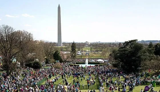 Multitud de personas reunidas en un jardín amplio con el Monumento a Washington al fondo