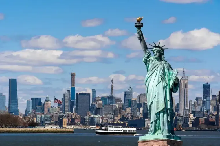 Freiheitsstatue vor der Skyline von Manhattan mit Ausflugsschiff auf dem Wasser