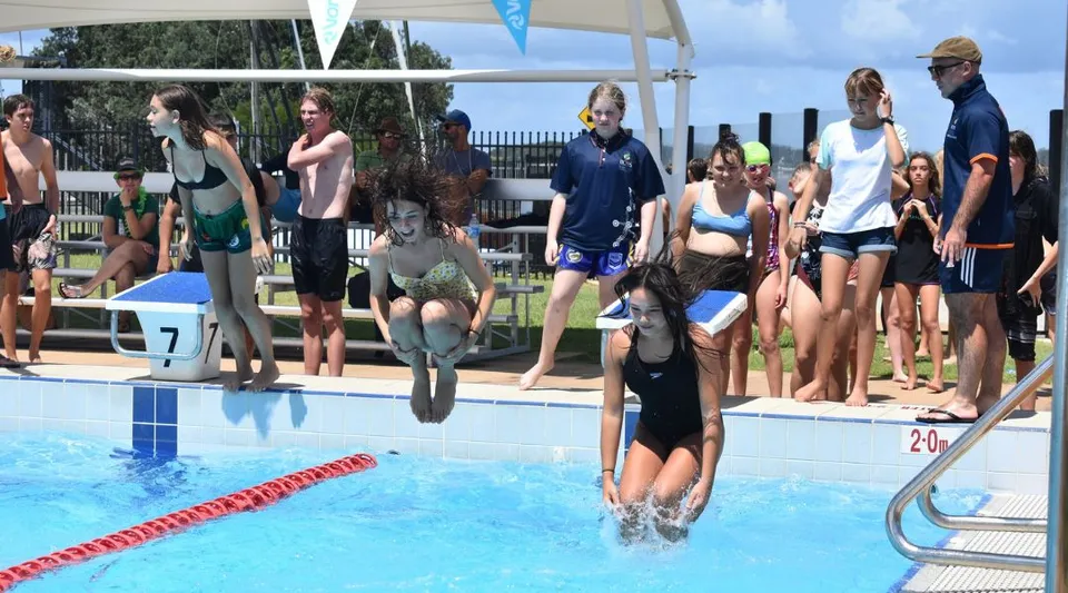 Un gruppo di studenti della Ballina Coast High School si trova a bordo piscina e alcuni sono in acqua.
