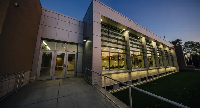 Das moderne mehrstöckige Gebäude der Northeastern Wisconsin Lutheran High School mit Glaswänden steht beleuchtet auf einer Grasfläche.