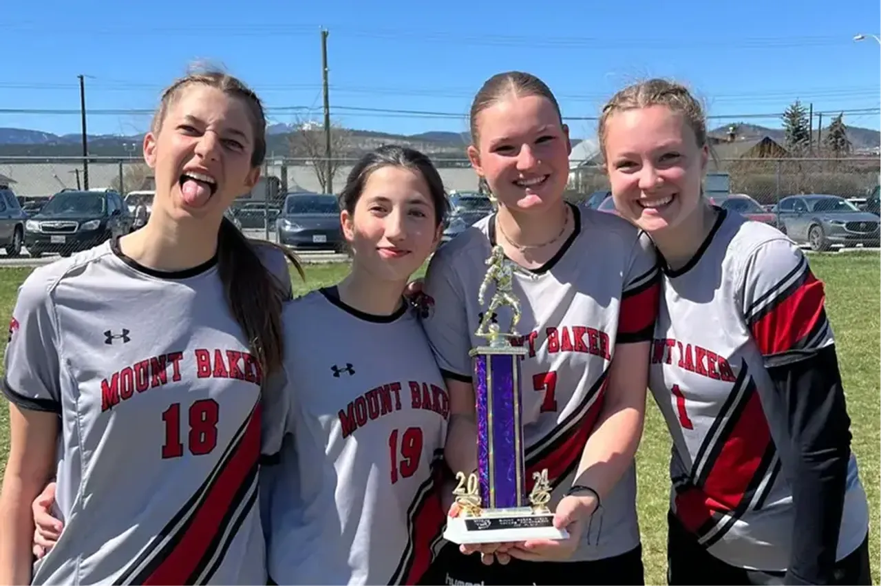 Quattro studentesse in maglia sportiva della squadra mostrano un trofeo su un campo