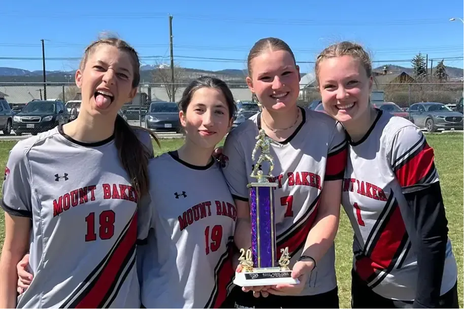 Quattro studentesse in maglia sportiva della squadra mostrano un trofeo su un campo