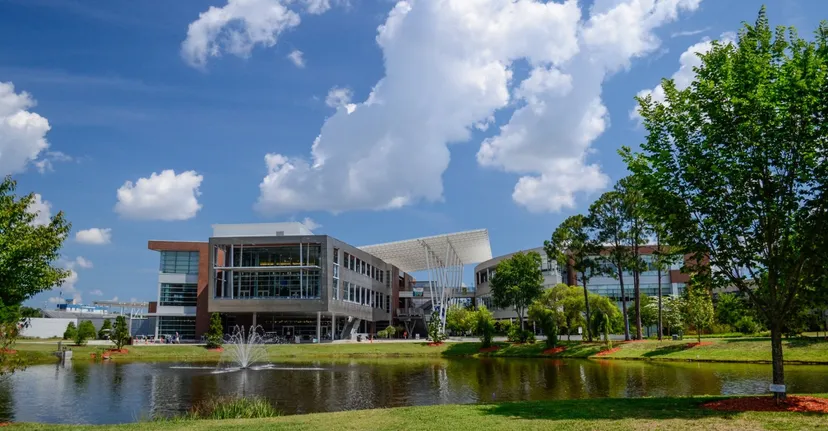 Edificio con facciata in vetro nel campus della University of North Florida, circondato da un paesaggio verde con laghetto e fontana.