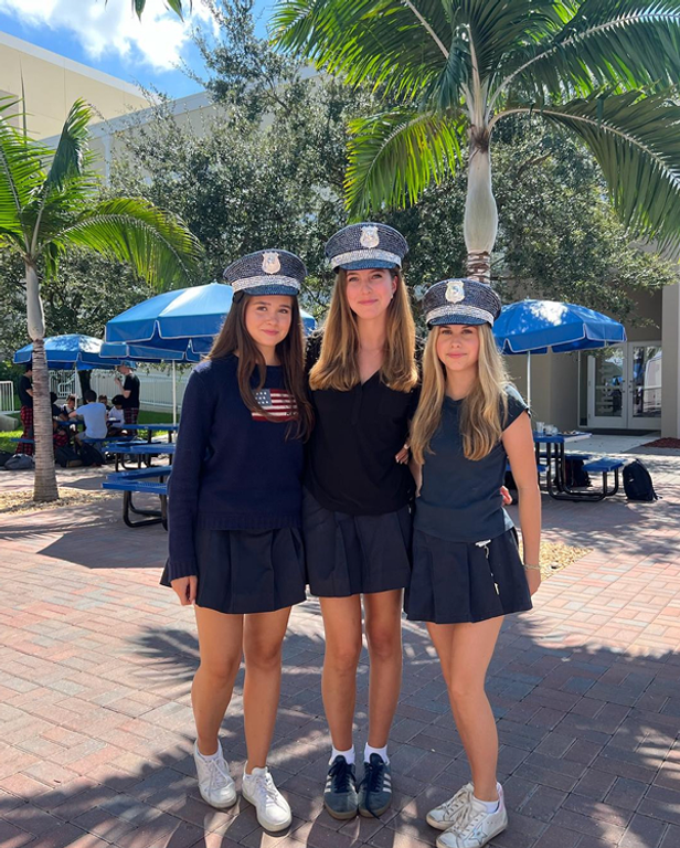 Tre studentesse posano sorridenti con cappelli a tema tra le palme del campus di una scuola americana