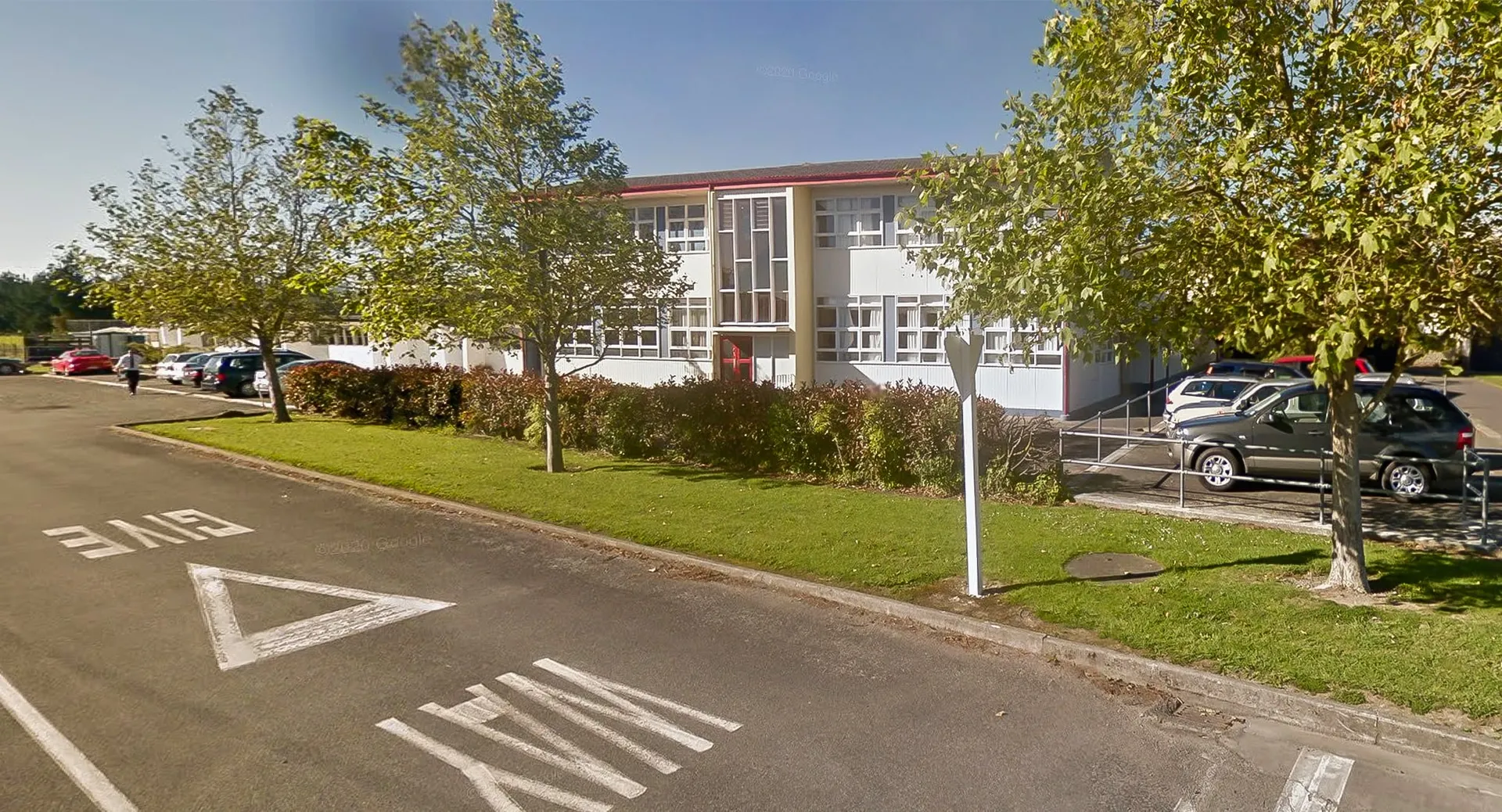 Il moderno edificio a più piani del Kuranui College è circondato da alberi e si affaccia su una strada con segnaletica orizzontale.