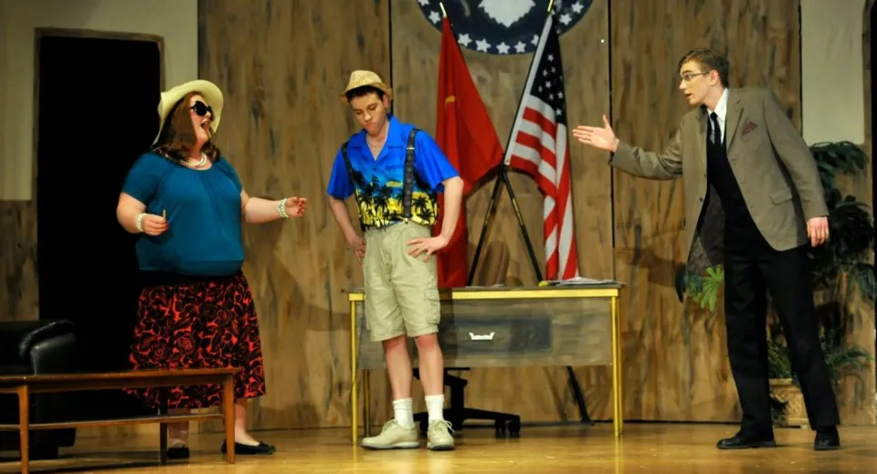 Tre persone sono in piedi davanti a una parete in legno con la bandiera americana durante una presentazione alla Colonel By Secondary School.