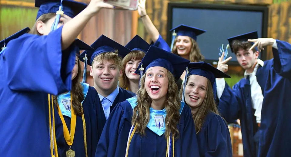 Un gruppo di diplomati della St. John’s-Ravenscourt School in toghe blu è insieme all'aperto davanti a una staccionata in legno.