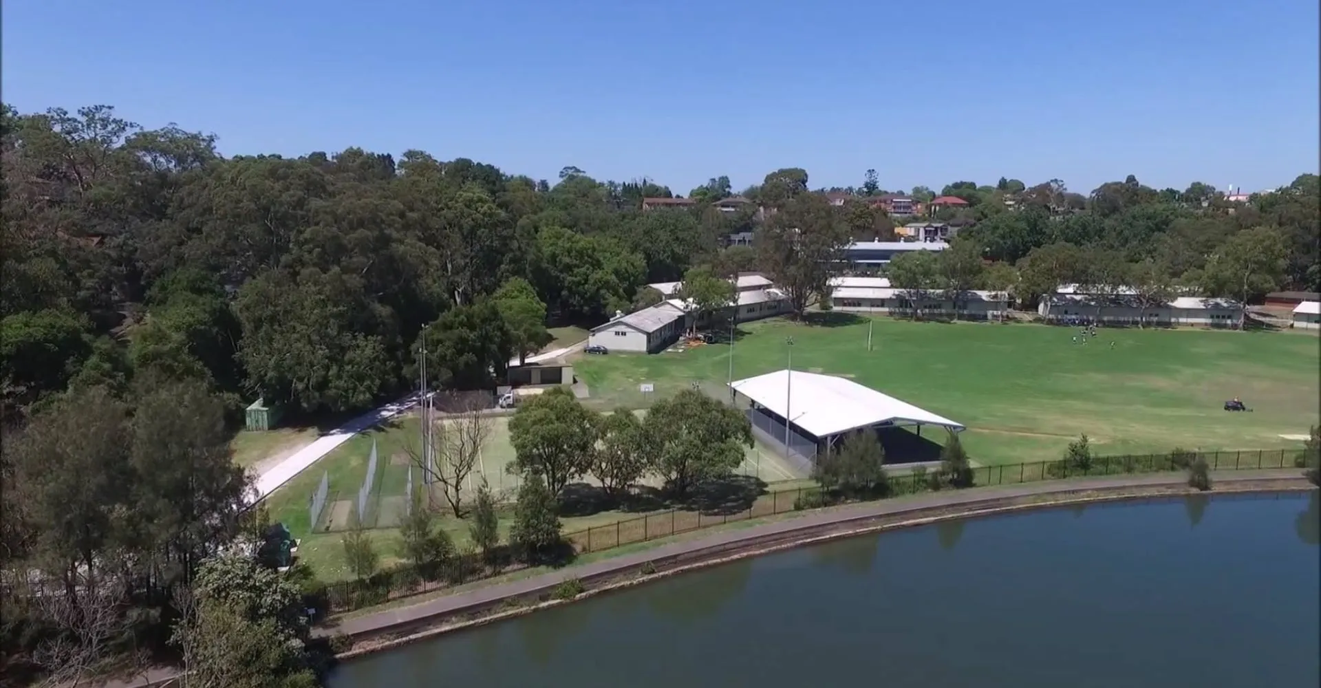 Un campo verde con un piccolo lago e edifici sullo sfondo nel campus della Hunters Hill High School.