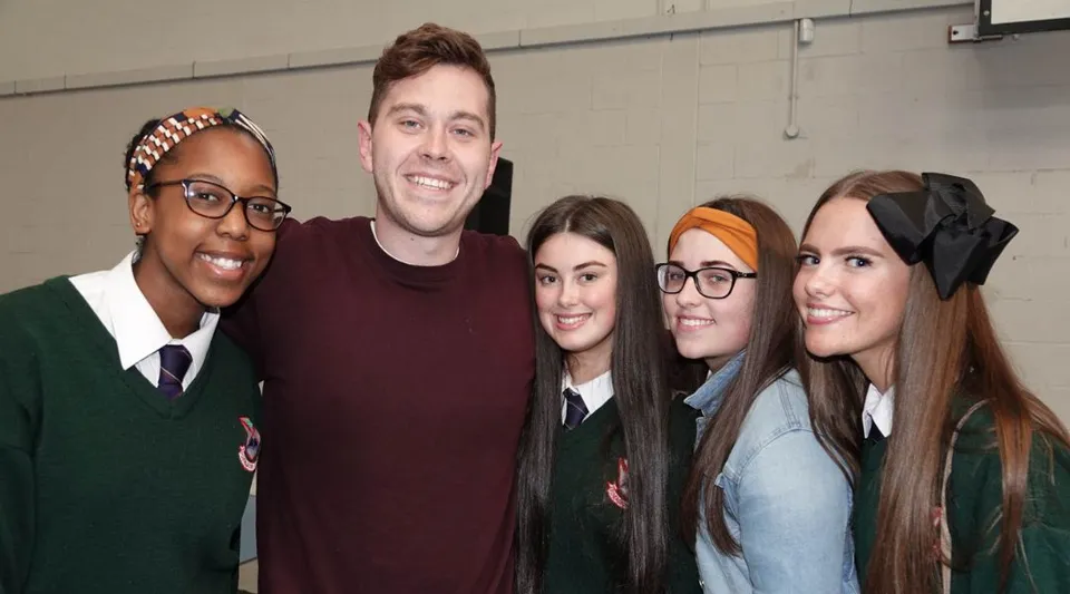 Cinque studenti posano insieme nella Palmerstown Community School davanti a una parete semplice.