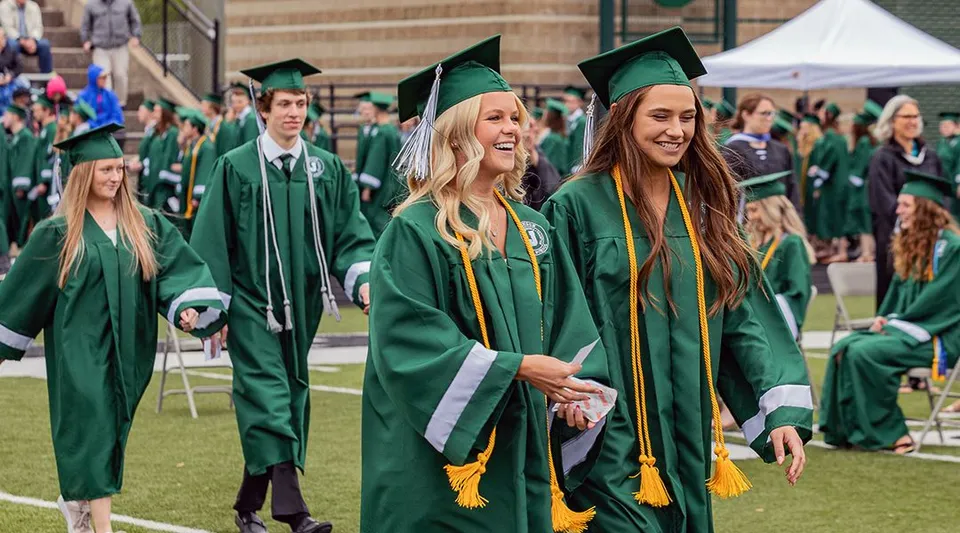 Diplomati e diplomate delle Jenison Public Schools sono in piedi su un prato all'aperto con toga e tocco verdi.