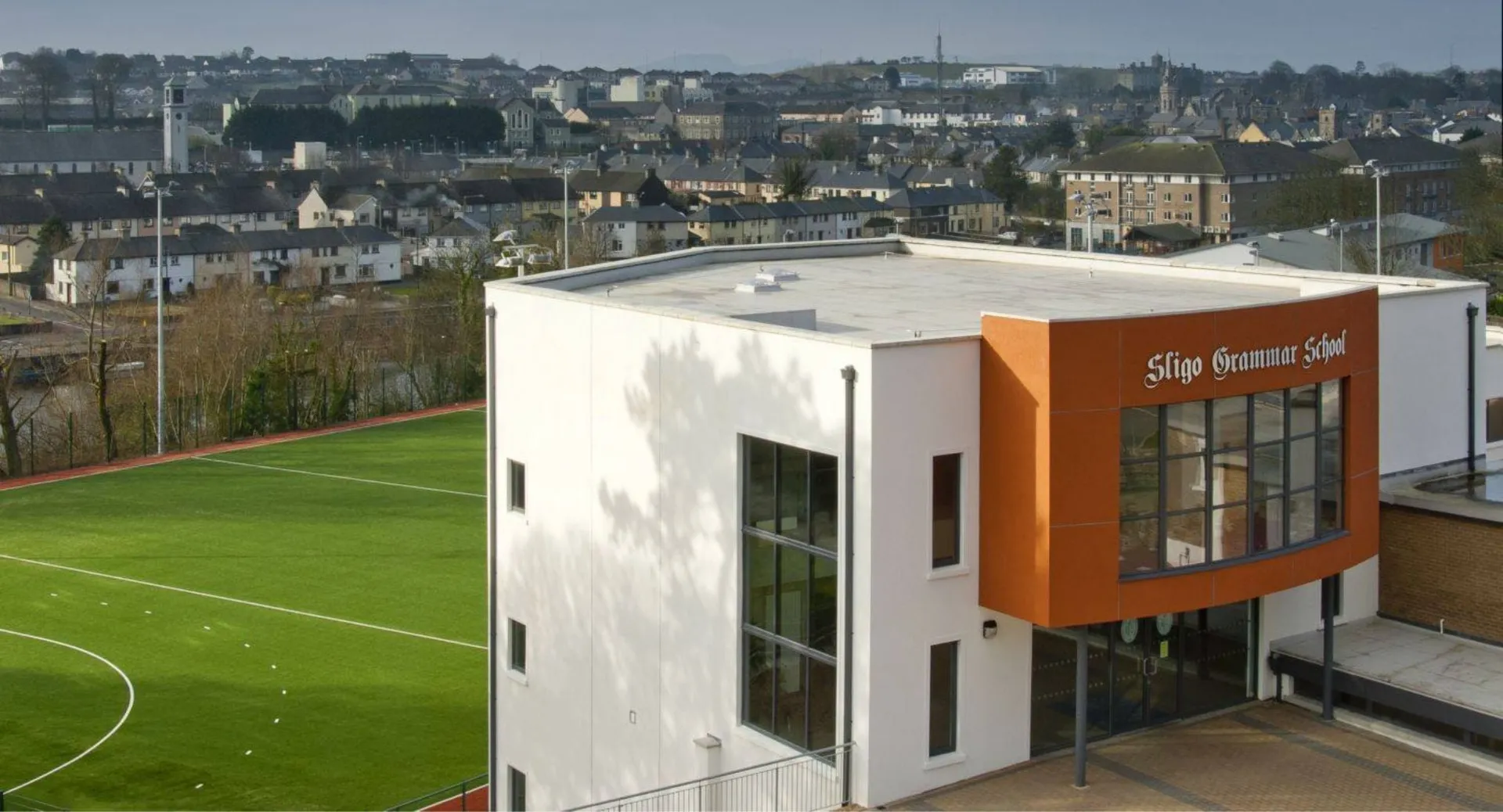 L'edificio moderno della Sligo Grammar School con grandi finestre si affaccia su un verde campo da calcio con lo sfondo della città.