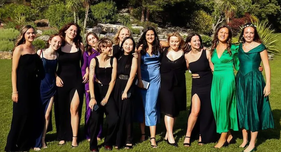 Un gruppo di studentesse della International Bilingual School of Provence in eleganti abiti da sera si trova in un ambiente verde e naturale.