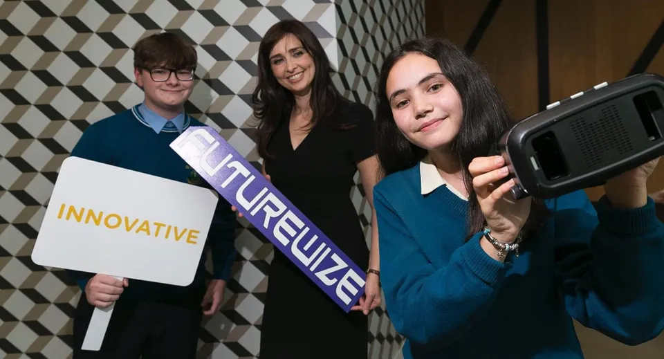 Tre studentesse della St. Tiernan’s Community School sono in piedi davanti a una parete decorata con un cartello 'Innovative'.