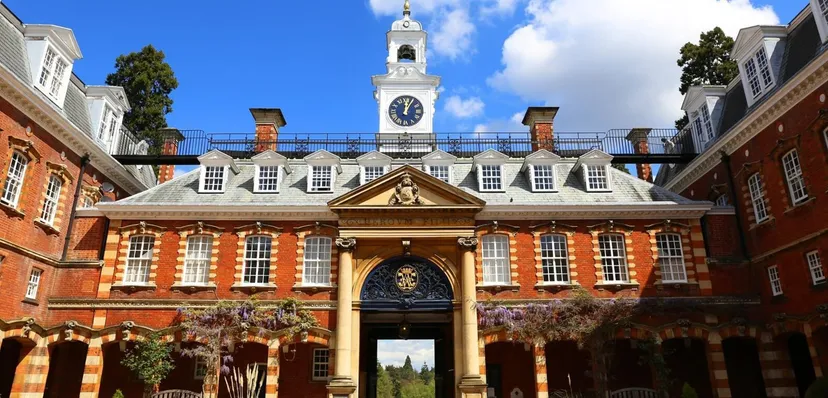 L'edificio in mattoni con la torre dell'orologio della Wellington School è circondato da alberi verdi e si staglia contro un cielo azzurro e limpido.