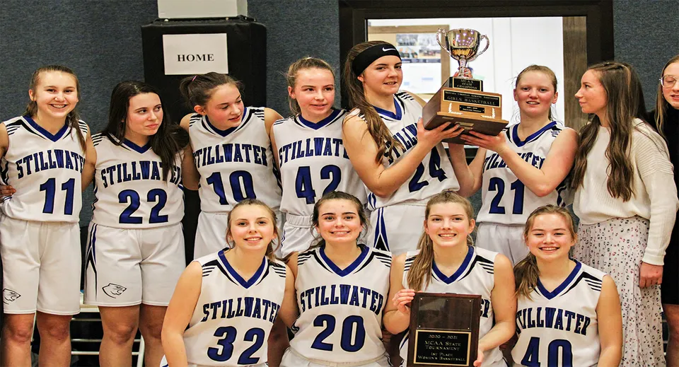 Un gruppo di giovani giocatrici di basket della Stillwater Christian School festeggia la vittoria con un trofeo negli spogliatoi.