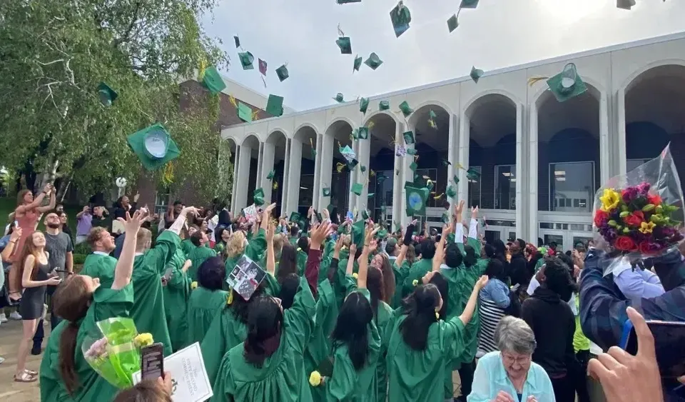 Un gruppo di persone in abbigliamento verde si riunisce davanti all'edificio della Martin Luther High School con archi e colonne.